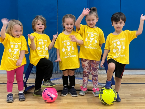 Five young children in YMCA t-shirts playing indoor soccer
